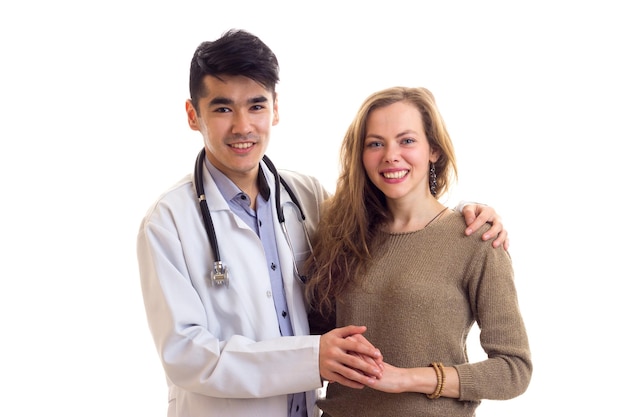 Jonge aantrekkelijke dokter in witte jurk met stethoscoop op zijn nek die jonge mooie vrouw omhelst