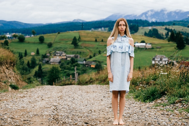 Foto jonge aantrekkelijke elegante blonde meisje in blauwe romantische jurk poseren op het platteland