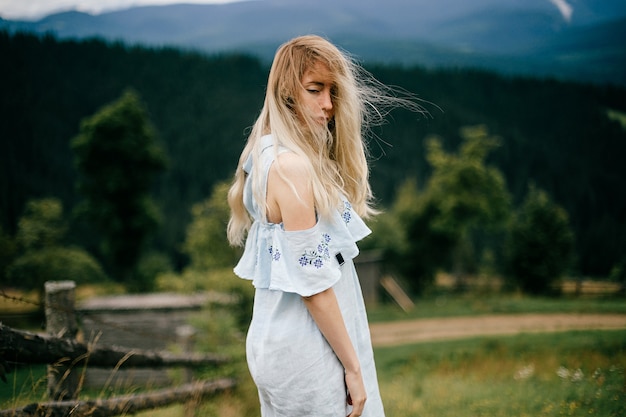 Jonge aantrekkelijke elegante blonde meisje in blauwe romantische jurk poseren over schilderachtig landschap