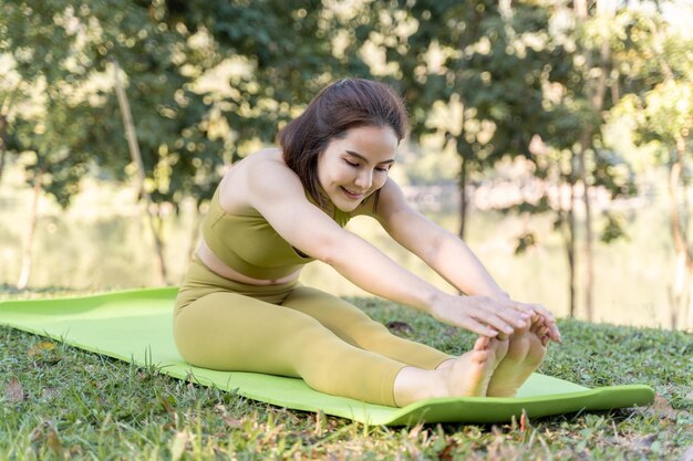 Jonge aantrekkelijke en actieve vrouw die zich uitstrekt op een groene yogamat tijdens het beoefenen van haar ochtendyoga