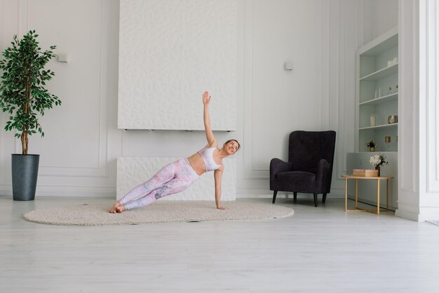 Jonge aantrekkelijke glimlachende vrouw die yoga beoefent, aan het trainen is, sportkleding draagt, beha, thuis