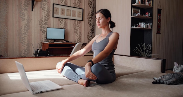 Foto jonge aantrekkelijke glimlachende vrouw die yoga beoefent terwijl ze in halve lotus-oefening zit