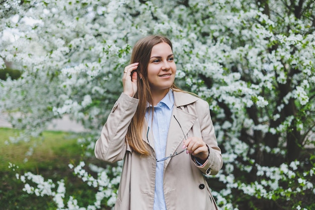 Jonge aantrekkelijke glimlachende vrouw met een mooi kapsel op een achtergrond van bloeiende roze appelboom Selectieve fokus bij vrouw