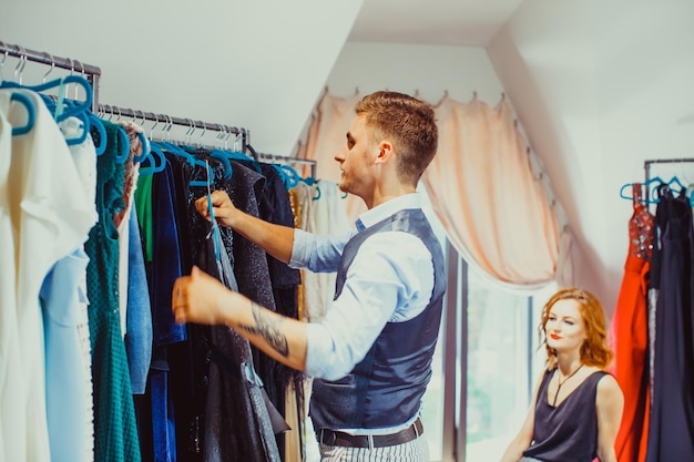 Jonge aantrekkelijke man aan het werk als modestylist en koper voor rijke vrouwen. Kledingkoper adviseert zijn klant om kleding te kopen