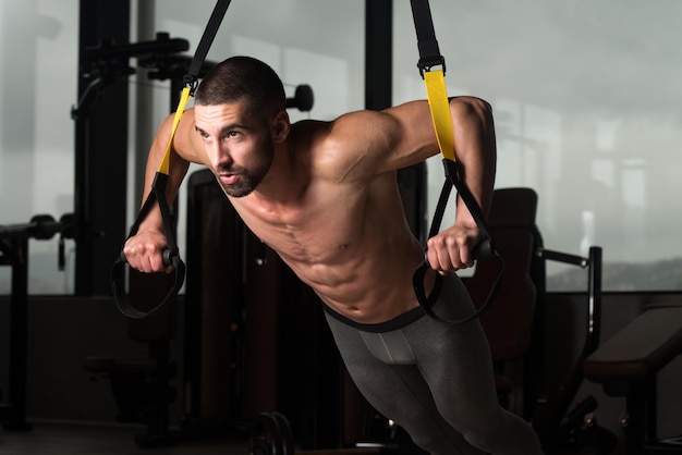 Jonge aantrekkelijke man die traint met Trx-fitnessriemen