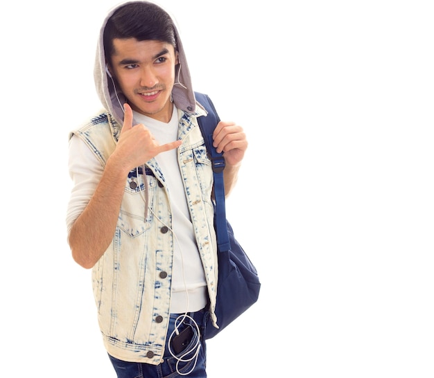 Jonge aantrekkelijke man in spijkerjasje met rugzak met koptelefoon op witte achtergrond in studio