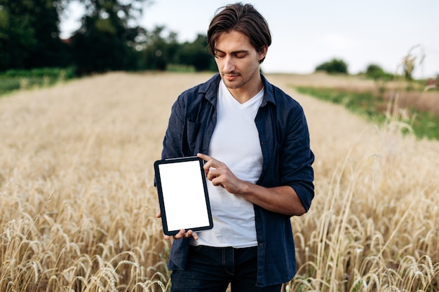 Jonge, aantrekkelijke man met een tablet in zijn handen op een tarweveld