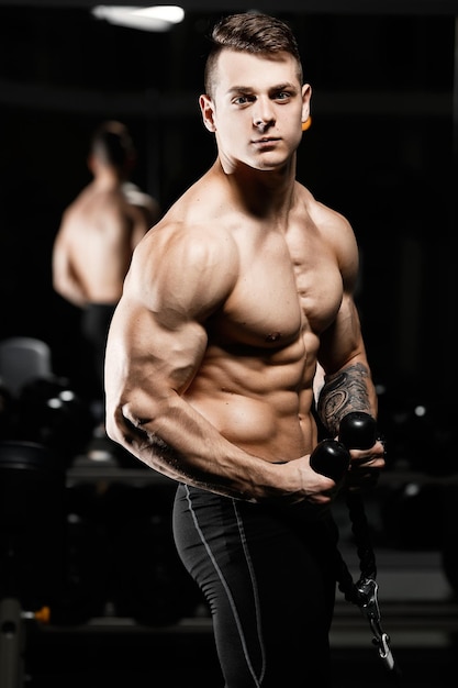 Jonge aantrekkelijke mannelijke bodybuilder toont spieren in de sportschool De atleet Professional Light