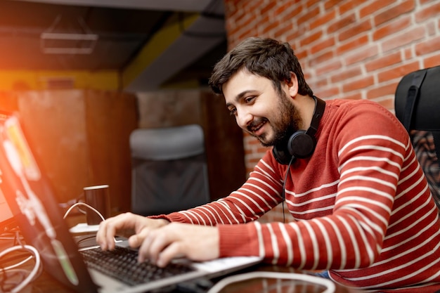 Jonge aantrekkelijke ontwerper die op kantoor werkt. Knappe man die lacht op de computer.