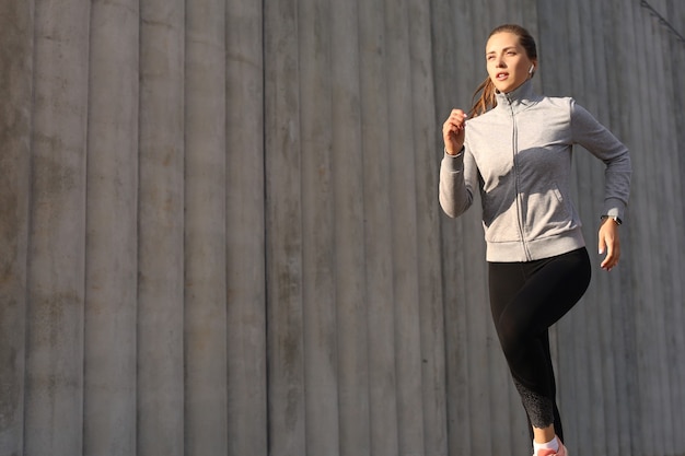 Jonge aantrekkelijke sportieve fitness vrouw loopt tijdens het sporten buiten bij zonsondergang of zonsopgang in de stad.