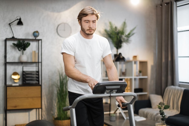 Jonge aantrekkelijke sportieve man in wit t-shirt met ochtendtraining in modern licht appartement