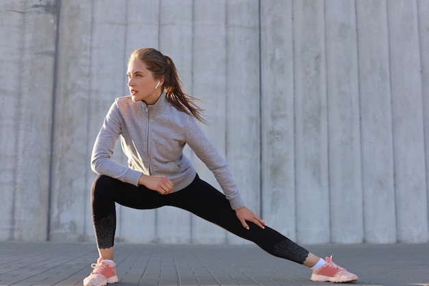 Jonge aantrekkelijke sportieve meid die buiten opwarmt, stretching doet bij zonsondergang of zonsopgang in de stad.