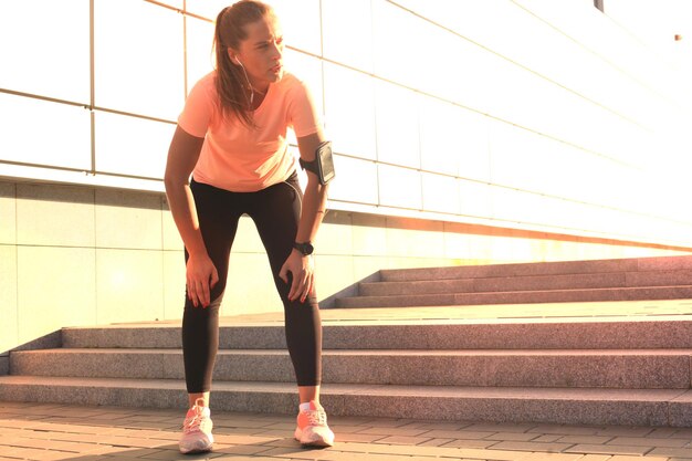 Jonge, aantrekkelijke sportieve meid die rust na een intensieve avondwandeling buiten bij zonsondergang in de stad