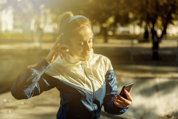 Jonge aantrekkelijke sportvrouw in sportkleding met koptelefoon luistert naar muziek in het sportpark.