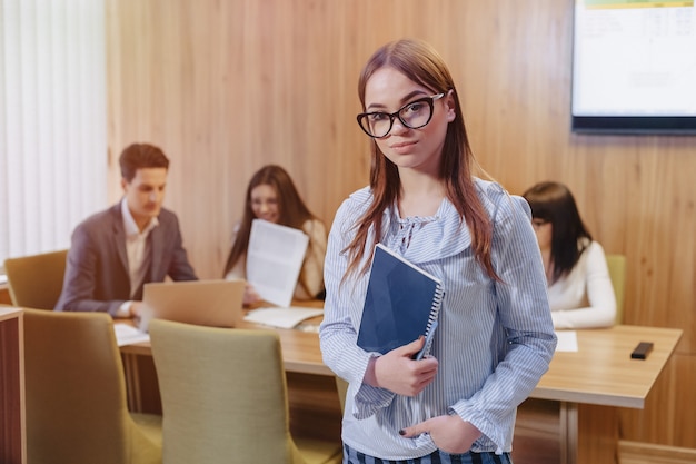 Jonge aantrekkelijke stijlvolle kantoor werknemer meisje in glazen met een notebook in de handen van werkende collega's