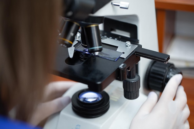 Jonge aantrekkelijke veterinaire werknemer in handschoenen met behulp van Microscoop voor het testen van bloedmonsters van dieren. Dierenarts arts op zoek naar Microscoop, close-up.