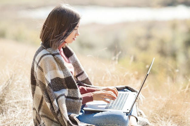 Jonge aantrekkelijke vrouw die aan laptop in openlucht werkt. Vrouw doet haar freelance werk op pc. Externe werknemer op vakantie.