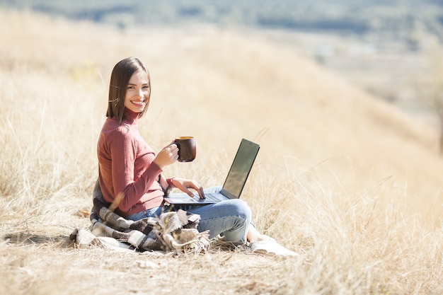 Jonge aantrekkelijke vrouw die aan laptop in openlucht werkt. Vrouw doet haar freelance werk op pc. Externe werknemer op vakantie.