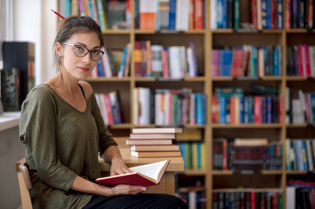 Jonge aantrekkelijke vrouw die een boek in een bibliotheek houdt