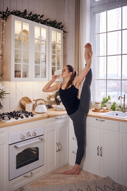 Jonge aantrekkelijke vrouw die yoga beoefent bij moderne keuken