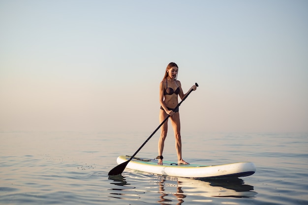 Jonge aantrekkelijke vrouw die zich op paddleboard bevindt