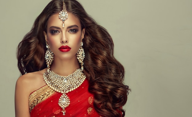 Jonge aantrekkelijke vrouw, gekleed in traditionele Indiase rode sjaal (dupatta) en handgemaakte sieradenset in "kundan-stijl". Perfect, dicht, golvend, vrij rondvliegend haar en make-up in "smoky eyes" -stijl.