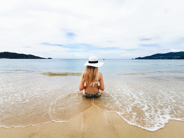 Foto jonge aantrekkelijke vrouw in een hoed op de kust van de blauwe overzeese leunend met een kokosnoot, thailand