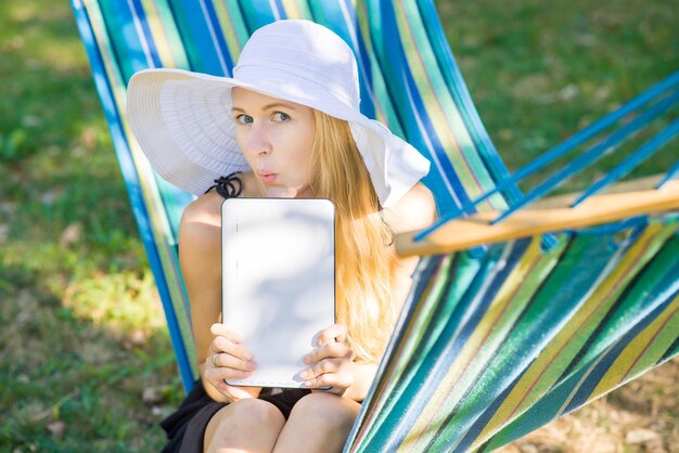 Jonge aantrekkelijke vrouw in hoed met behulp van een tablet op de hangmat in de tuin