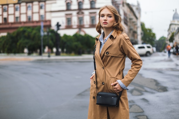 Jonge aantrekkelijke vrouw in trenchcoat met dromerig kleine zwarte dwarstas