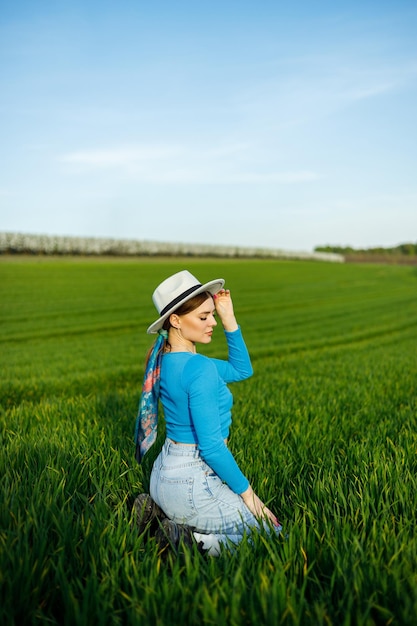 Jonge aantrekkelijke vrouw in witte hoed blauw shirt spijkerbroek poseren in zomer groen veld Kopieer lege ruimte voor tekst