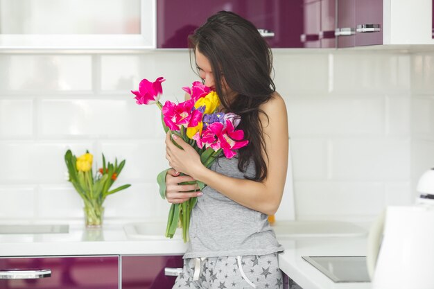 Jonge aantrekkelijke vrouw met bloemen. Dame op de keuken met tulpen. Huisvrouw in de ochtend die zich op de huiskeuken bevindt.