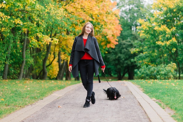 Jonge aantrekkelijke vrouw met haar teckel hond in haar armen buiten in zonsopgang in park in de herfst tijd