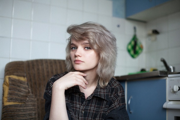 Jonge aantrekkelijke vrouw met kort haar zittend in vervallen fauteuil in oude vintage keuken