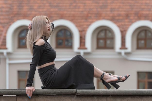 Jonge aantrekkelijke vrouw met lang blond haar draagt zwarte kleding lange rok en hakken Portret van stijlvol meisje buiten