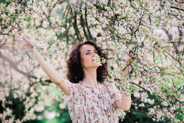 Jonge aantrekkelijke vrouw met lang krullend haar poseren in bloeiende lentetuin