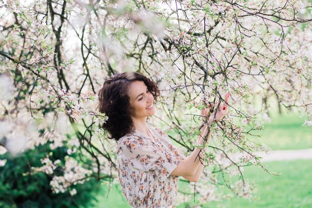 Jonge aantrekkelijke vrouw met lang krullend haar poseren in de bloeiende lentetuin, appelbomen