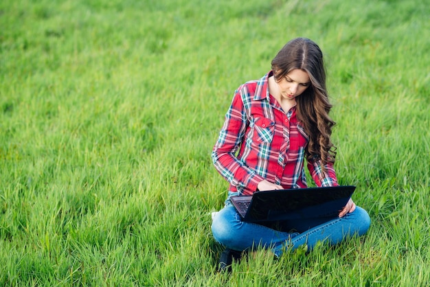 Jonge aantrekkelijke vrouw met laptop op het gras in bloeiende tuin