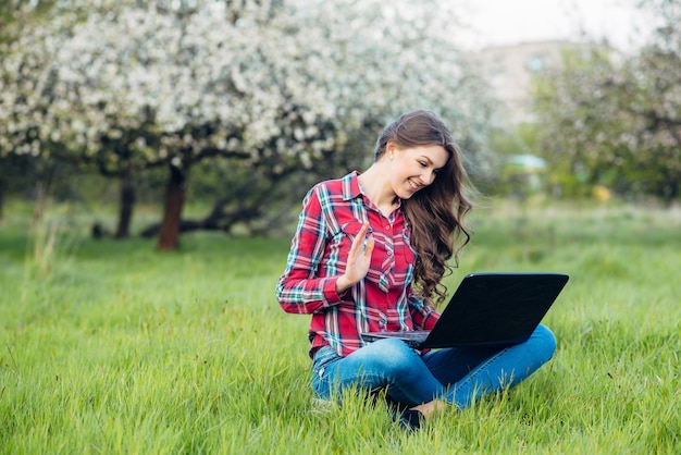 Jonge aantrekkelijke vrouw met laptop op het gras in bloeiende tuin