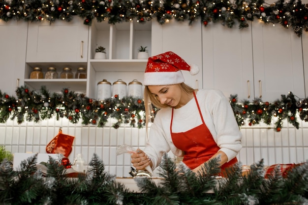 Jonge aantrekkelijke vrouw met rode schort en kerstmuts houdt poedersuiker in haar handen.