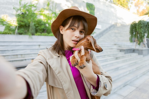 Jonge aantrekkelijke vrouw met teckel puppy in stadspark maakt selfie portret