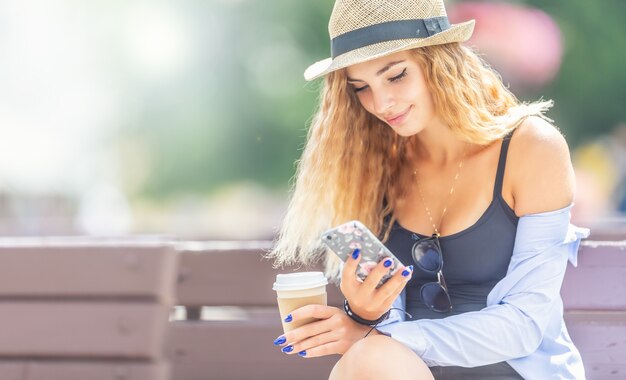 Jonge aantrekkelijke vrouw op parkbank met koffie die mobiele telefoon met behulp van.