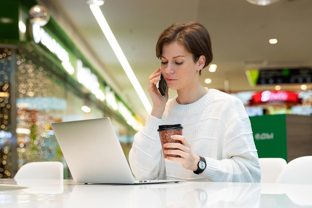 Jonge aantrekkelijke vrouw zit in een winkelcentrum aan een tafel en werkt op een computerlaptop