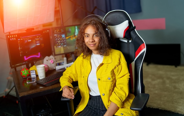 Jonge aantrekkelijke vrouw zitten in de buurt van tafel met computer. Videospelletjes op de computer. Meisje dat gaming-headset draagt.