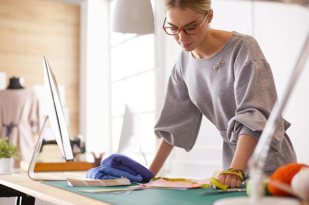 Foto jonge aantrekkelijke vrouwelijke modeontwerpers die op een bureau leunen en met een laptop werken