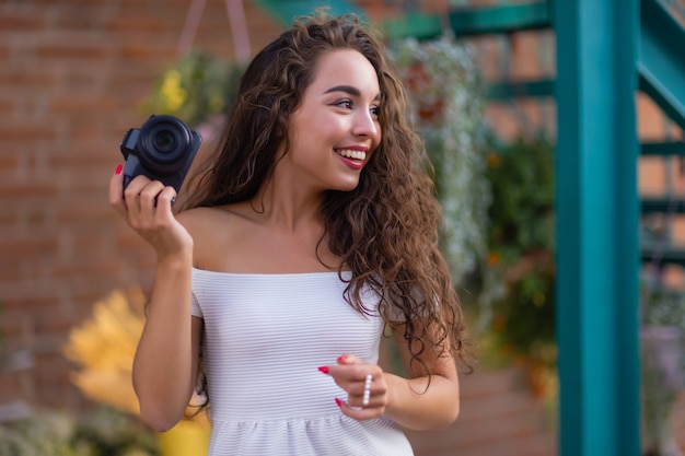 Jonge aantrekkelijke vrouwelijke student of toerist die een spiegelloze camera gebruikt tijdens het wandelen in de zomerstad wo...