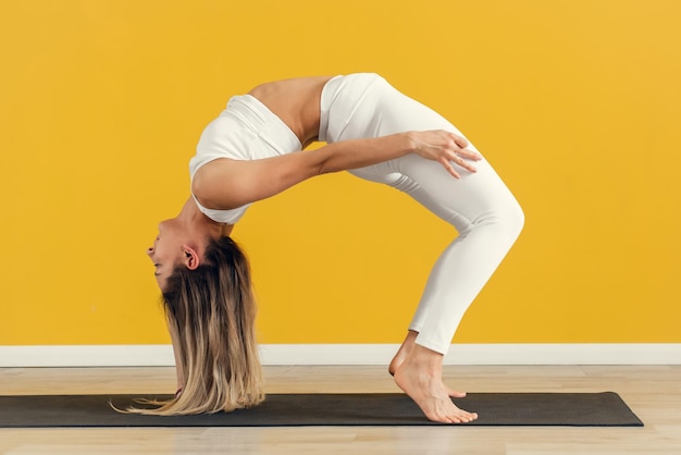 Jonge, aantrekkelijke yogi-vrouw die een brugoefening beoefent zonder armen die zich uitstrekken in Urdhva Dhanurasana-oefening op gele achtergrond