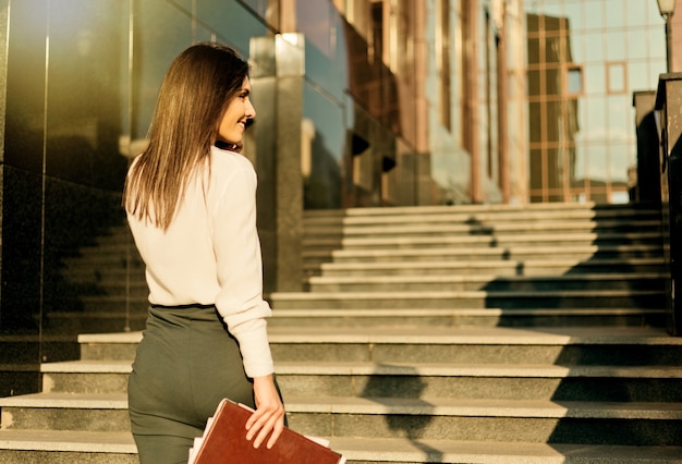 Jonge aantrekkelijke zakenvrouw in een blouse en een rok praat aan de telefoon. Bedrijfsconcept