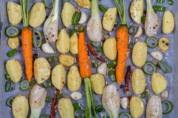 Foto jonge aardappelen wortels ui peper knoflook bereid op bakplaten voor het bakken in de oven bovenbeeld van dichtbij