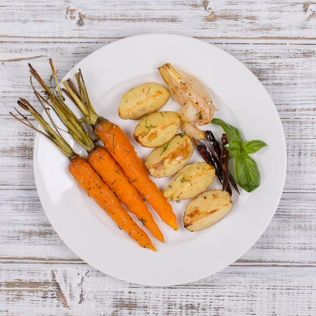 Jonge aardappelen wortels uien paprika's knoflook gebakken in de oven op het witte bord Bovenbeeld van dichtbij