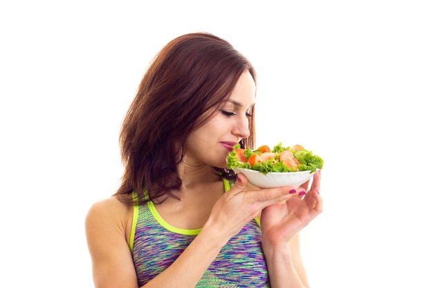 Jonge aardige vrouw in een gekleurde sporttop met een vork en bord met groene salade en tomaat